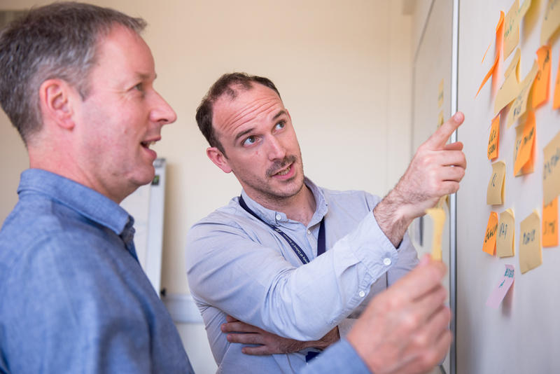 Two men looking at a whiteboard covered in post-it notes.