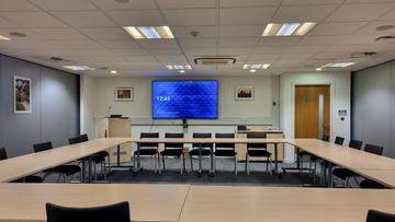 A large meeting room showing a screen and camera setup for hybrid meetings