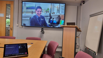 Person on screen in hybrid meeting room