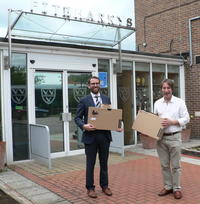Photo of two people holding laptop boxes outside a school