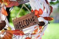 A white wreath with autumn leaves tucked in and a small sign in the centre saying 'welcome'