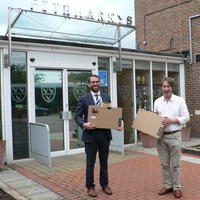 Photo of two people holding laptop boxes outside a school